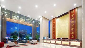 A hotel lobby with a reception desk, seating area, and large windows offering a view of the cityscape.