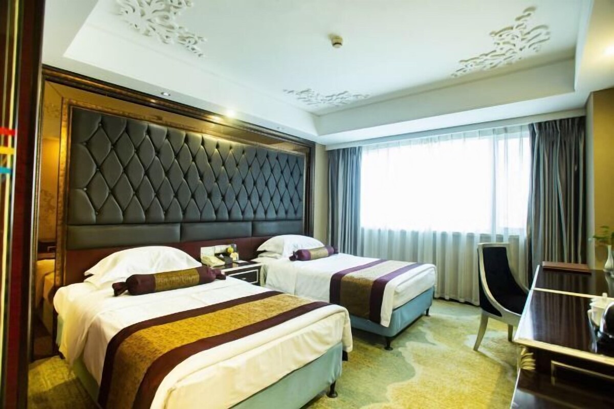 A hotel room with two beds, a large tufted headboard, a desk, and a chair.
