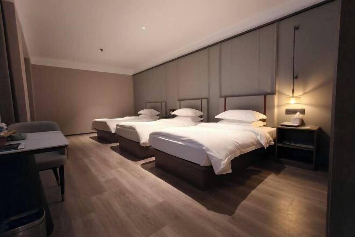 A hotel room with two beds, a desk, and a nightstand with a lamp.