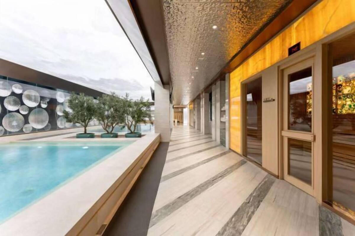 A modern hotel corridor with a pool, a decorative wall with circular patterns, and a wooden finish on the right side.