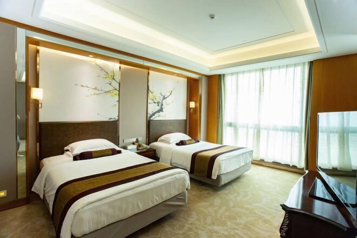 A hotel room with two beds, a desk, and a large window with curtains.