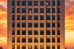 A high-rise building with a grid of windows and a sunset sky in the background.