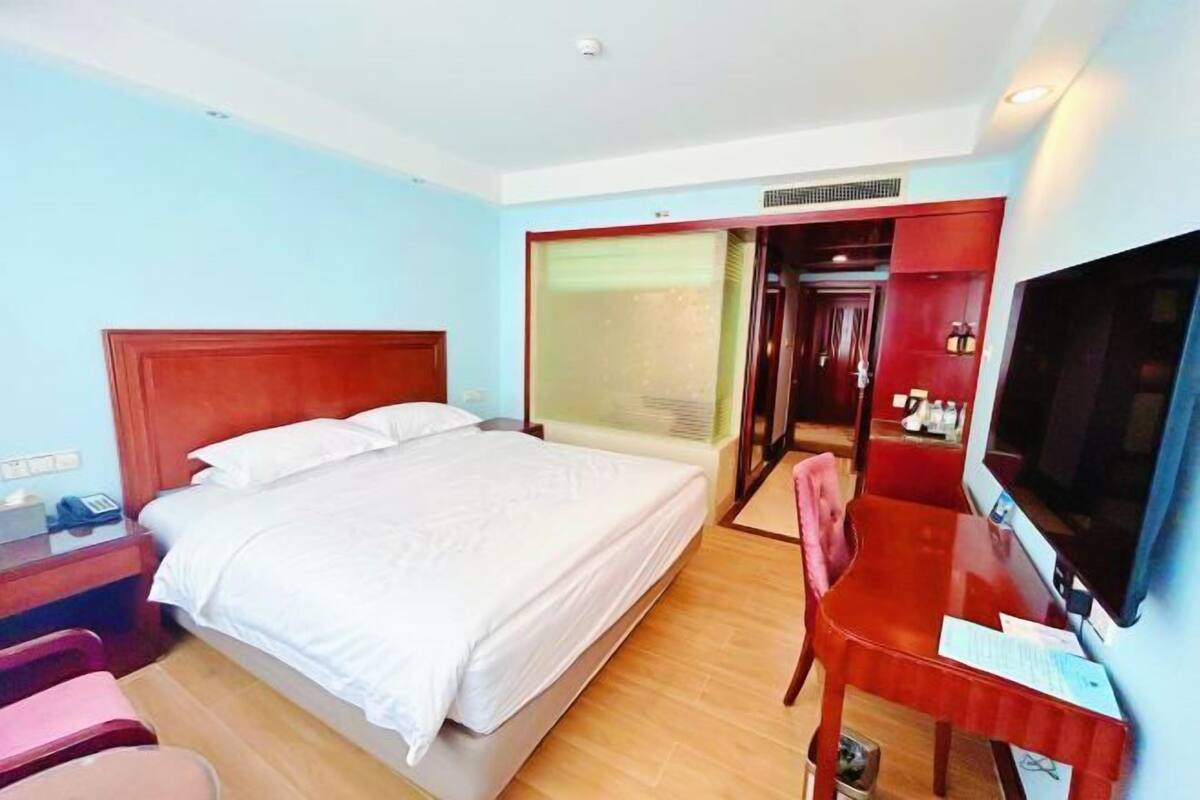 A hotel room with a bed, a desk with a computer, a TV, and a sliding door leading to a bathroom.