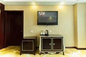 A room with a flat-screen TV mounted on the wall, a small cabinet with a coffee maker, and a door.