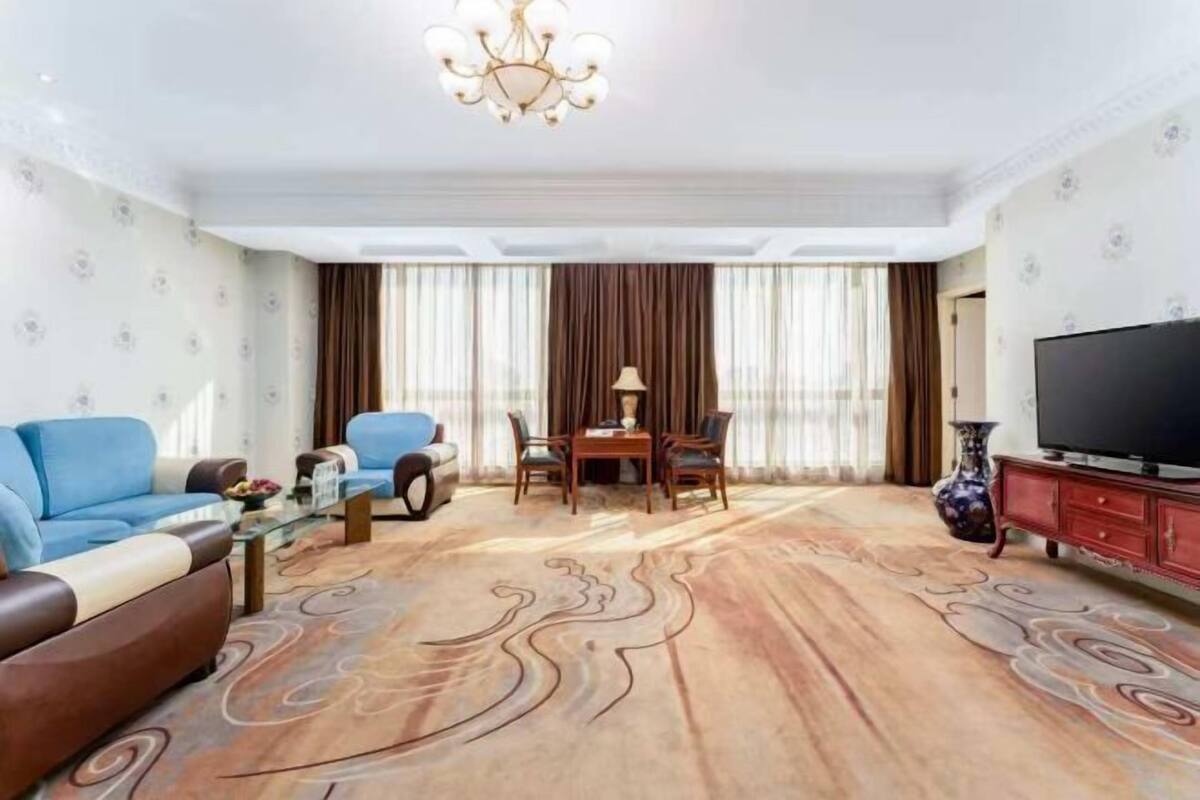 A living room with a sofa, a coffee table, a TV, a chandelier, and a patterned rug.