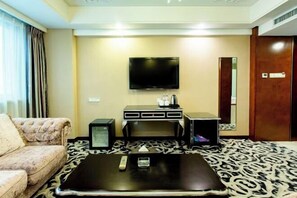 A hotel room with a flat-screen TV mounted on the wall, a sofa, a coffee table, and a patterned carpet. - Mei Li Hua Hotel (Dezhou)