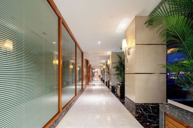 A corridor with a glass wall, a marble floor, and a plant on the right.