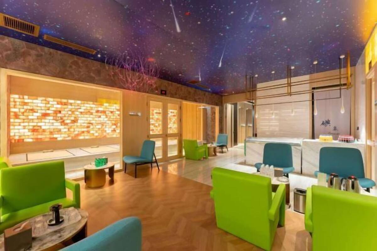 A modern lounge area with green seating, a brick wall display, and a starry ceiling.