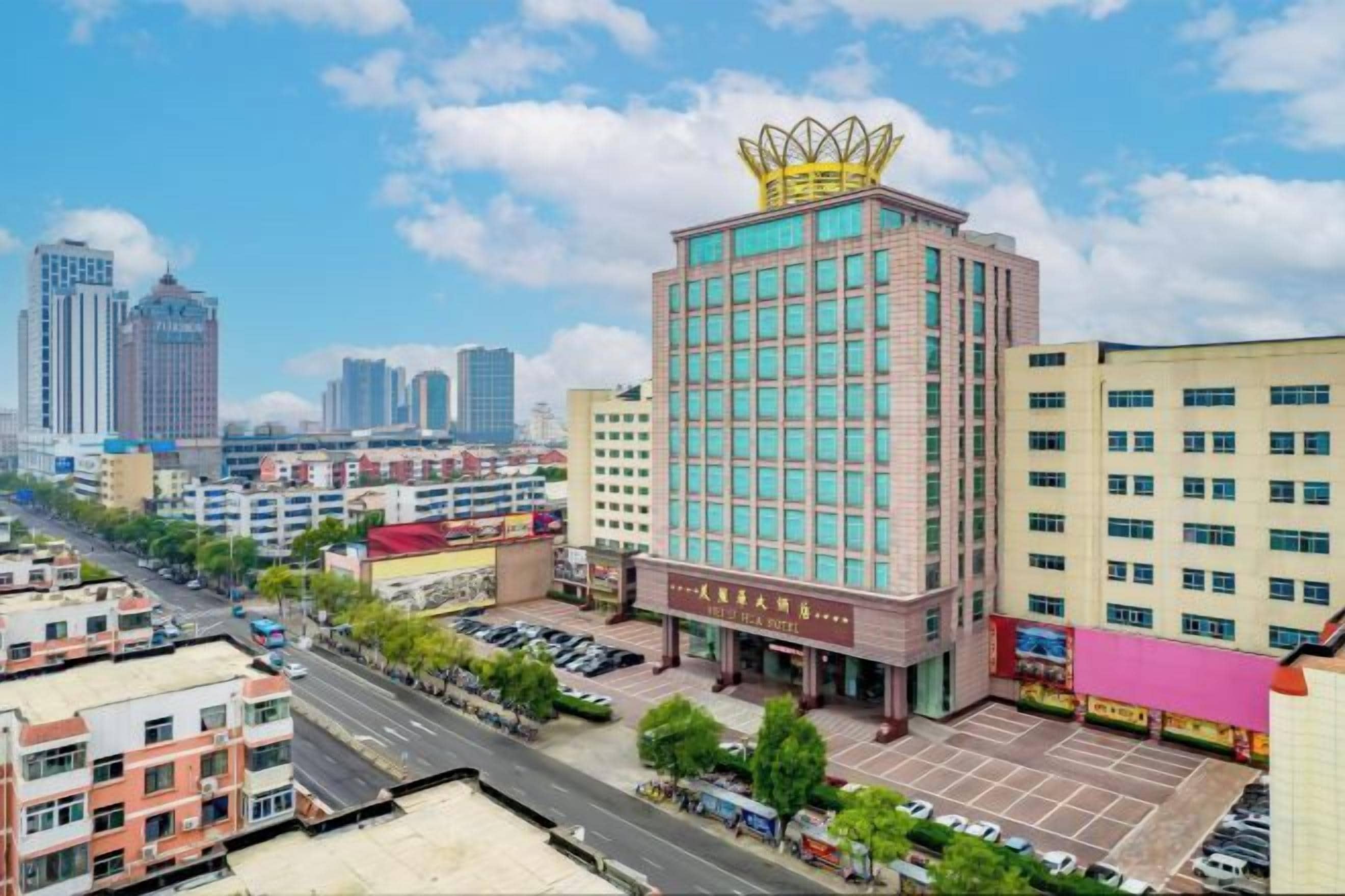 Un hotel a più piani con una struttura prominente a forma di corona sulla sommità, circondato da altri edifici e un parcheggio.