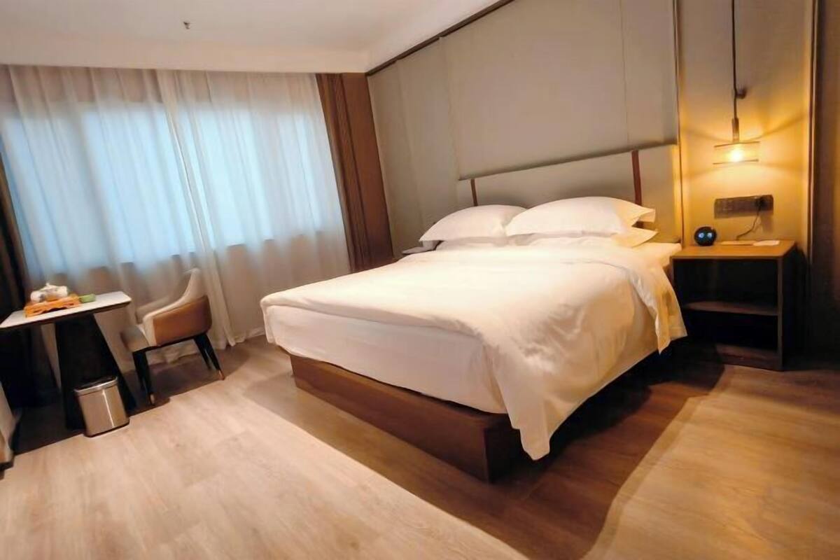A hotel room with a bed, a bedside table, a chair, a desk, and a window with curtains.