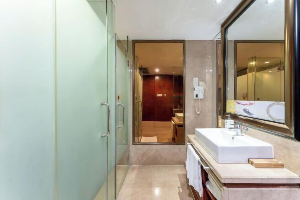 A modern bathroom with a large mirror, a white sink, and a glass shower enclosure.