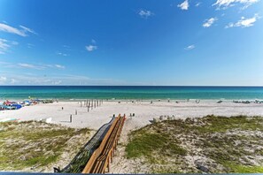 A beach with a wooden walkway leading to the shore, clear blue sky, and calm sea.