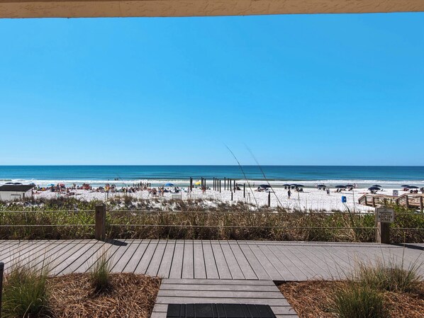 A beach view with a wooden boardwalk leading to the sand, a sign warning to keep off dunes, and a clear blue sky.