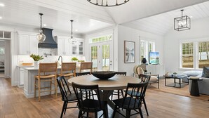 Une cuisine spacieuse avec des meubles blancs, un grand îlot central et un coin repas comprenant des chaises noires et une table en bois.
