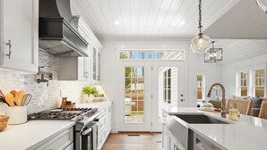 Une cuisine moderne avec des meubles blancs, une cuisinière à gaz et un grand îlot central doté d’un évier.