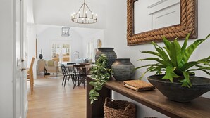 Un intérieur moderne avec une table à manger en bois, des chaises, un lustre et un grand miroir au mur.