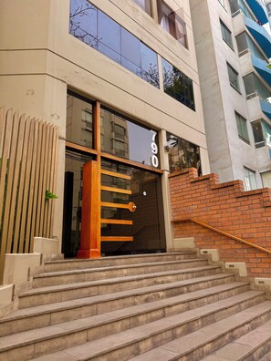 A building with a double staircase leading to a glass entrance, a brick wall, and a number '790' sign. - Beautiful ocean view! Spacious and elegant apartment, ideal for families (Miraflores)