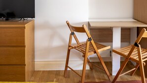 A room with a TV on a wooden stand, two wooden chairs, and a white wall. - Cosy Studio in Earls Court Flat 17 (London)