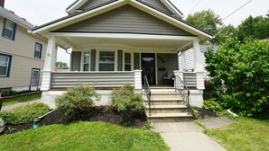 A two-story house with a front porch, a staircase, and a small garden area. - Cozy 3 Bedroom Home (Elyria)