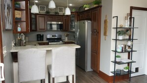 A kitchen with wooden cabinets, a stainless steel refrigerator, a double sink, and a bar stool. - Cozy 3 Bedroom Home (Elyria)
