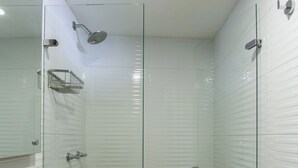 Un baño moderno con cabina de ducha de vidrio, paredes cubiertas de azulejos blancos y suelo de madera.