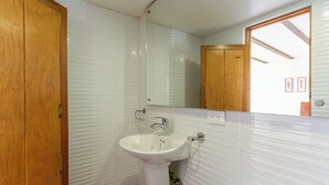 Un baño con lavamanos blanco, puerta de madera y un espejo sobre el lavamanos.