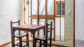 Un comedor con mesa y sillas de madera, techo blanco y piso de baldosas.