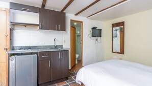 Habitación compacta con kitchenette, una cama, televisor y espejo.