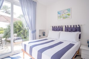 Un dormitorio con cama, mesita de noche, ventana con cortinas y un cuadro en la pared.
