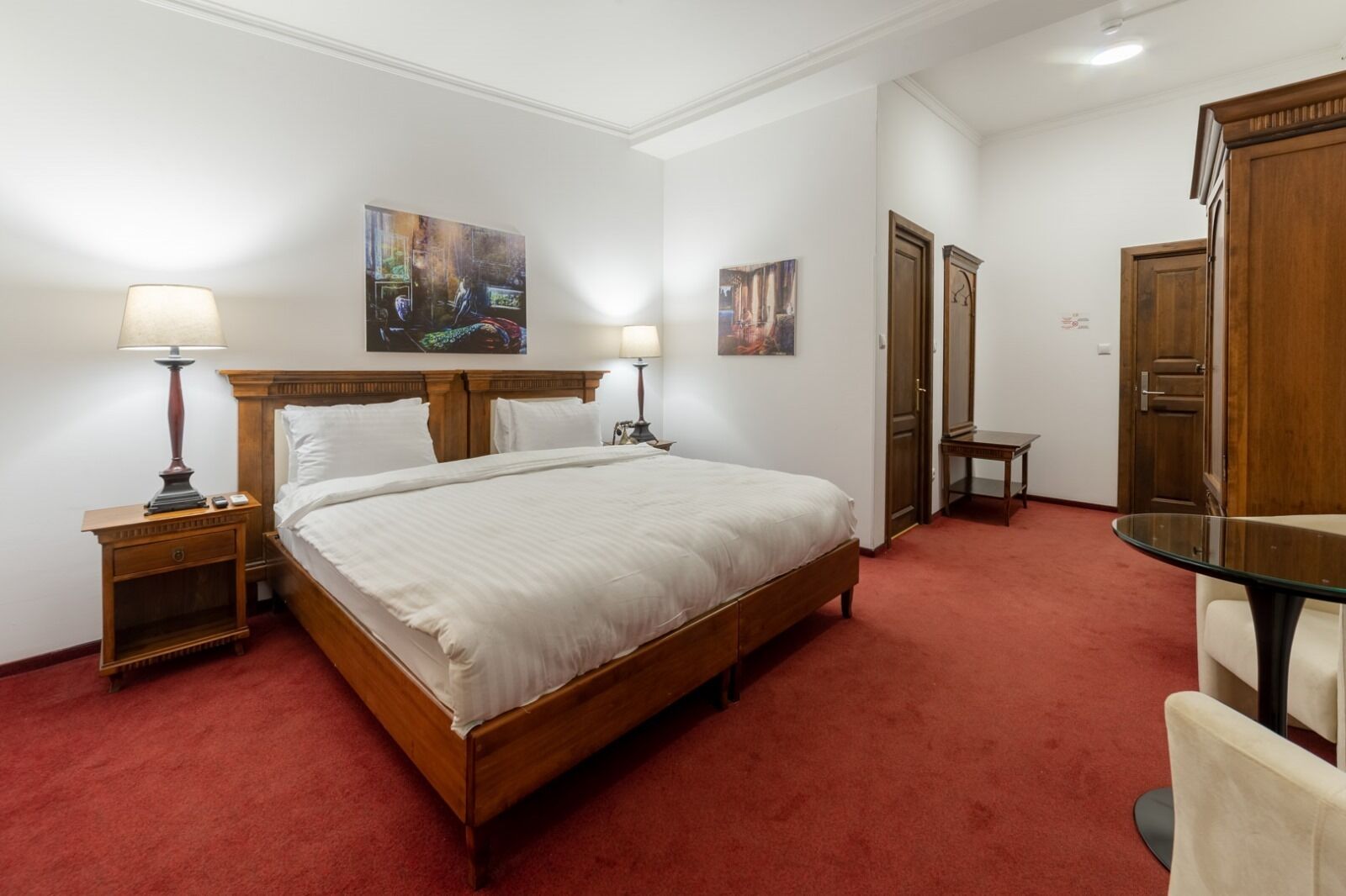 Une chambre d’hôtel avec un grand lit, deux tables de chevet avec des lampes, un bureau et deux portes.