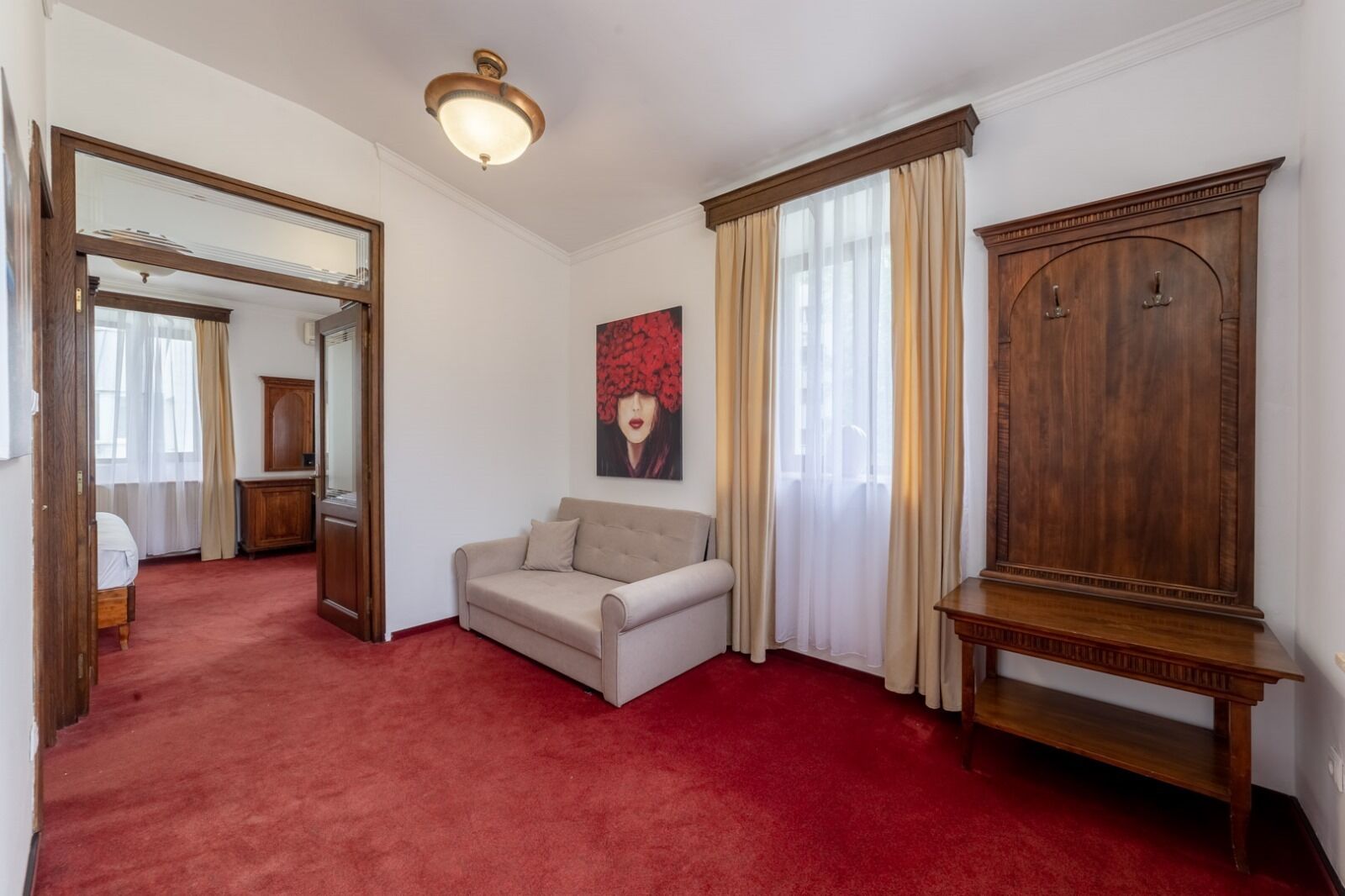 Ein Zimmer mit rotem Teppich, einem beigen Sofa, einem Holzschrank und einem großen Spiegel.