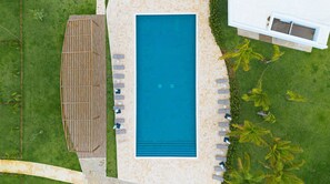 Vista aérea de un área de piscina con terraza de madera, sillas de descanso y una pared de piedra.