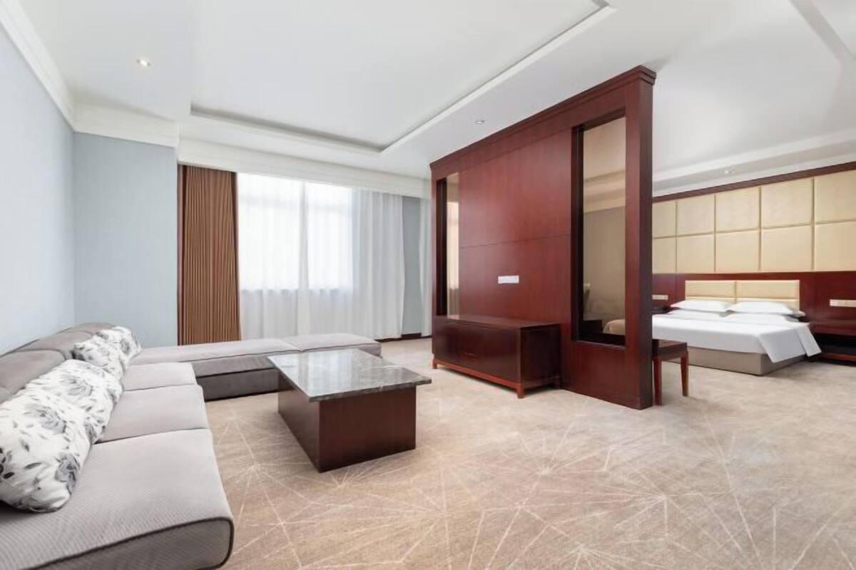 Een hotelkamer met een bank, een bed, een houten kledingkast, een kleine tafel en een groot raam.