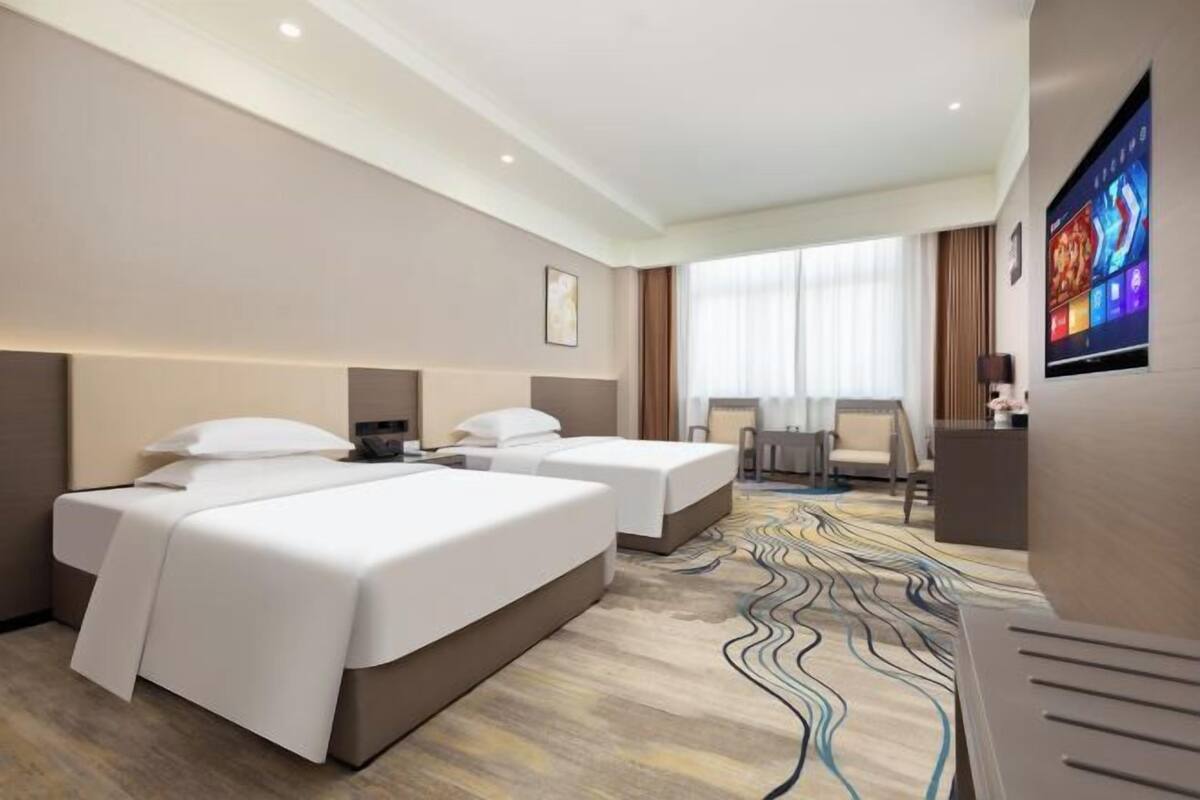 Een hotelkamer met twee bedden, een bureau, een televisie en een groot raam met gordijnen.