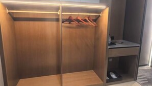 A modern closet with wooden doors, a hanging rack, and a small table with a laptop. - GreenTree GEM International Hotel (Zaozhuang Station Municipal Government) (Zaozhuang)