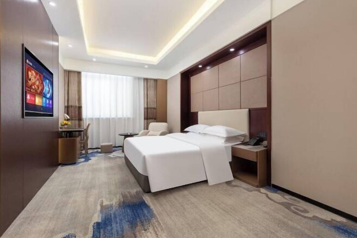 Een hotelkamer met een groot bed, nachtkastje, televisie bevestigd aan de muur en een raam met gordijnen.