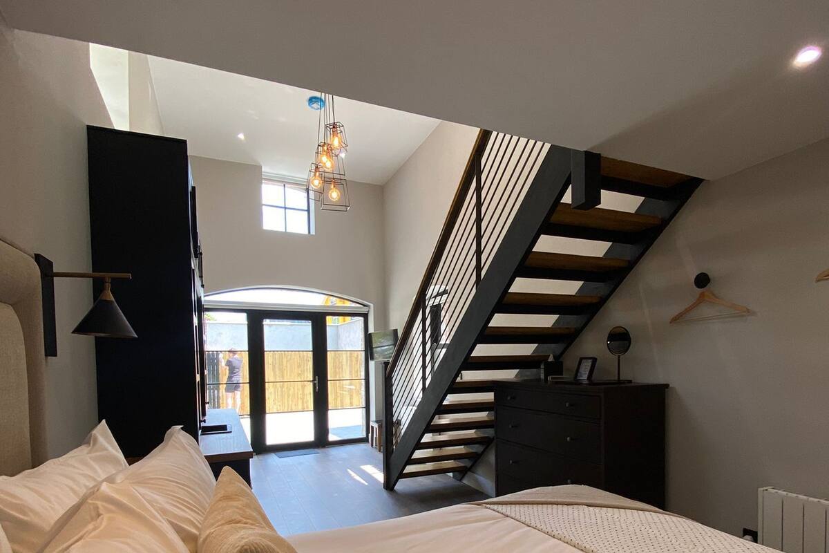 A bedroom with a large bed, a staircase, and a view of the outside.