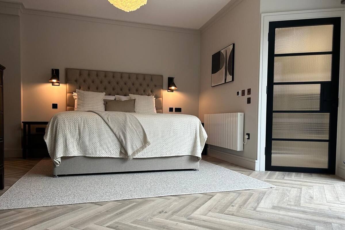 A bedroom with a large bed, two bedside lamps, a radiator, and a door with a window.