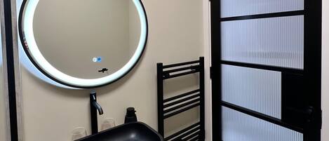 A bathroom with a round mirror, a black sink, and a towel rack.