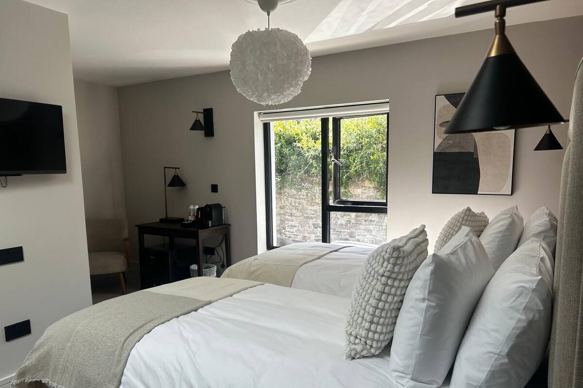 A bedroom with a bed, a desk, a chair, a television, and a window with a view of greenery.