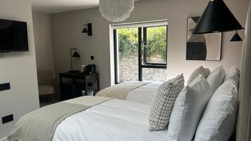A bedroom with a bed, a desk, a chair, a television, and a window with a view of greenery.