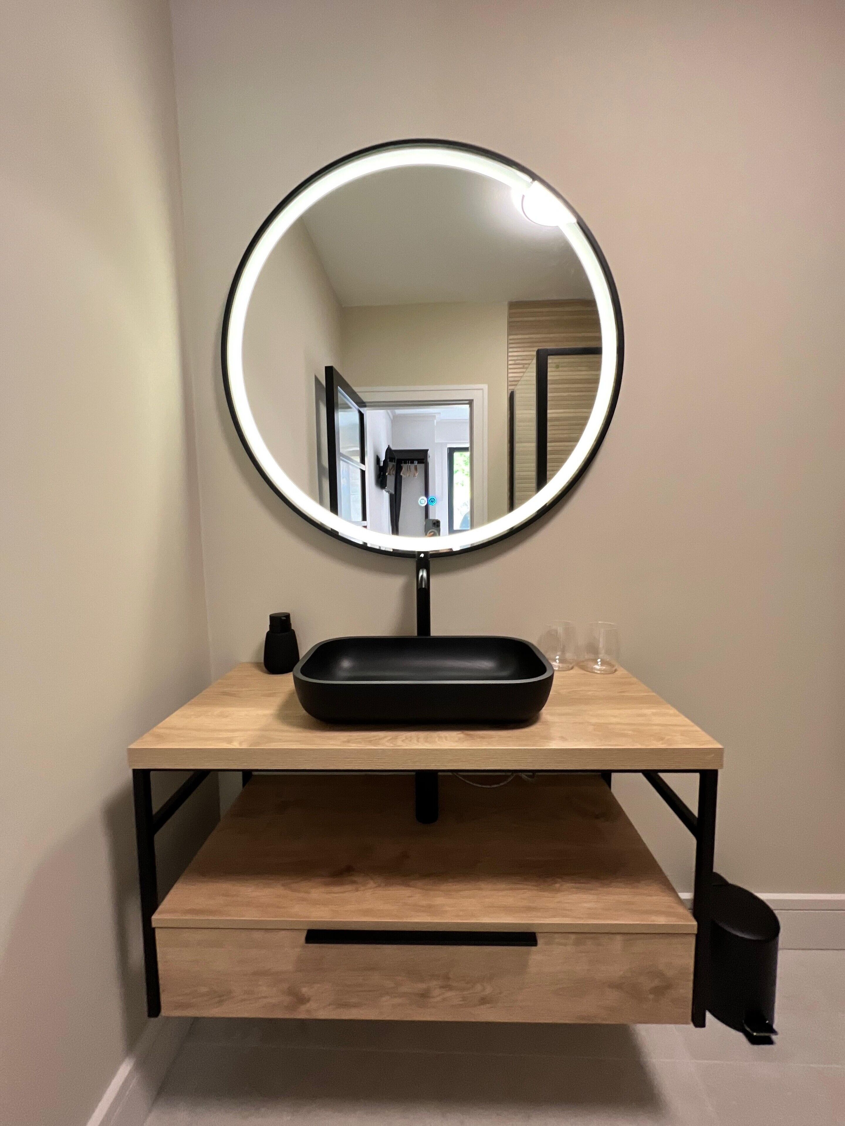Un tocador de baño con espejo redondo, lavamanos negro y encimera de madera.