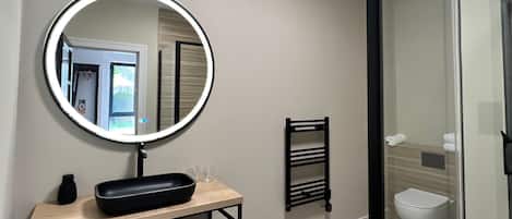 A modern bathroom with a round mirror, a wooden vanity, a glass shower enclosure, and a towel rack.