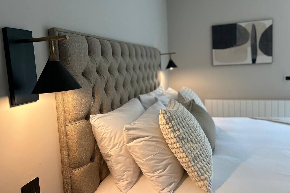 A bedroom with a tufted headboard, a bed with white bedding, and a black pendant lamp.