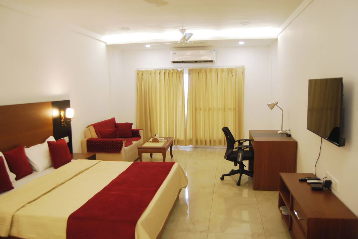 A hotel room with a large bed, a desk, a chair, a TV, and a window with curtains.