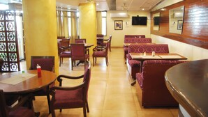 A restaurant with round tables and booths, wooden chairs, and a tiled floor. - Grey Pelican Tourist Resort (Yamunanagar)