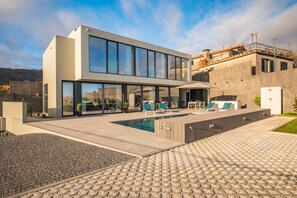 Een modern huis met een zwembad, buitenmeubilair en een grote glazen gevel.