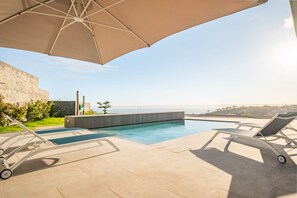 Un espace extérieur avec une piscine, des chaises longues et un grand parasol.