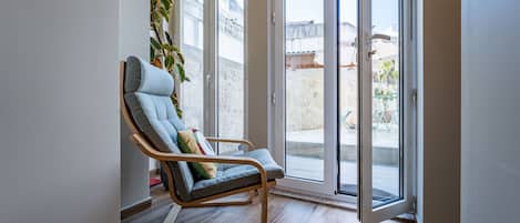 A modern room with a wooden floor, a blue cushioned chair with a pillow, and a sliding glass door leading to an outdoor area.
