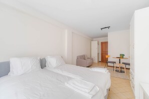 Une chambre d’hôtel avec deux lits, un canapé, une petite table avec des chaises et une porte donnant sur une autre pièce.